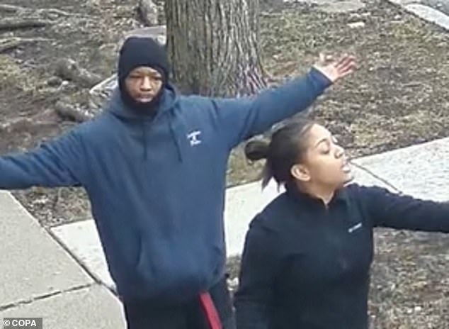 Leevon Smith stands behind the officer with his arms raised as she protects him from three other men